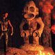 The main character from Far Cry 6 seen standing next to a monkey statue near a big fire in a temple.